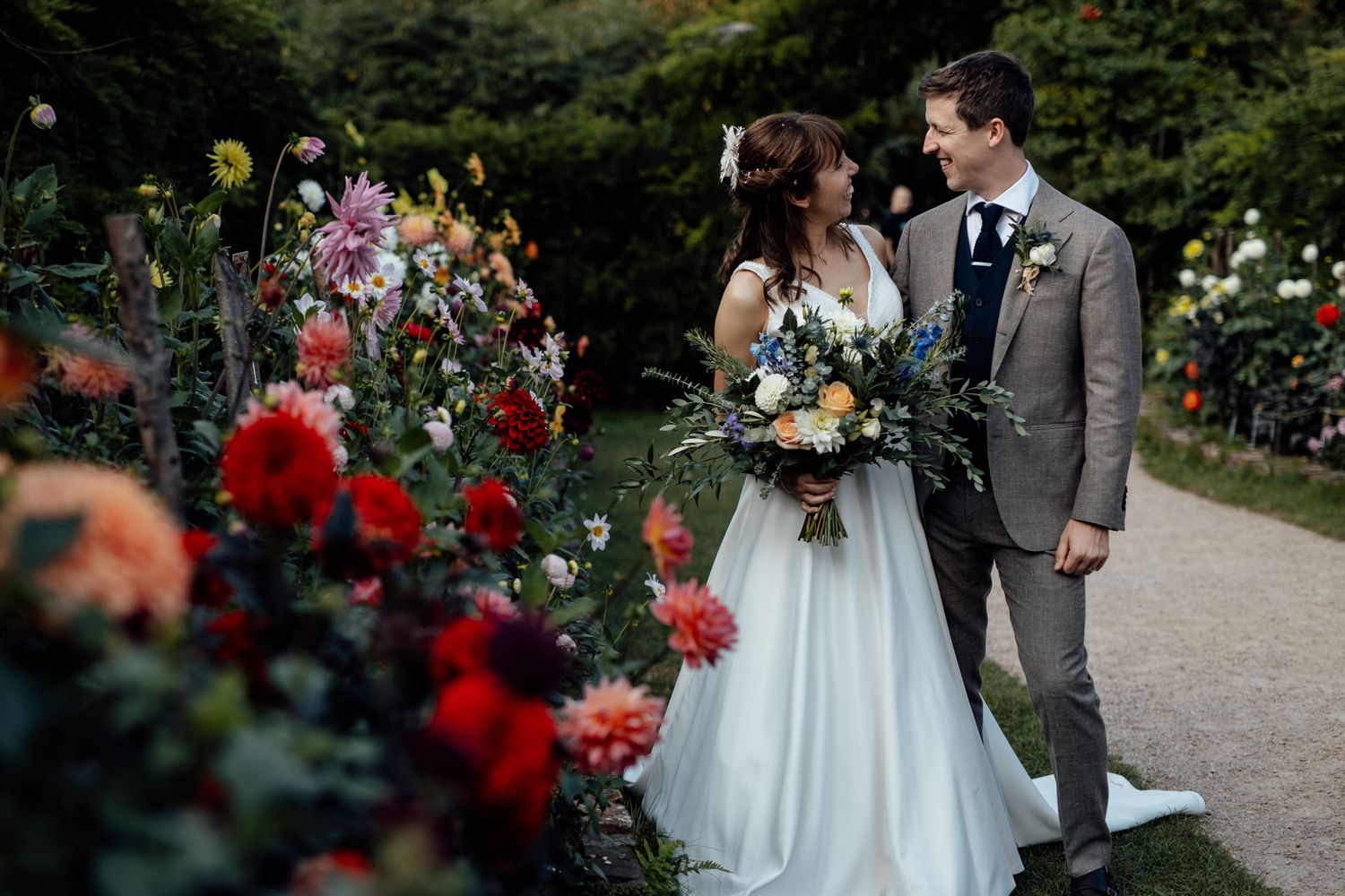 Couple poses together in a garden setting with vibrant red roses and summer flowers.