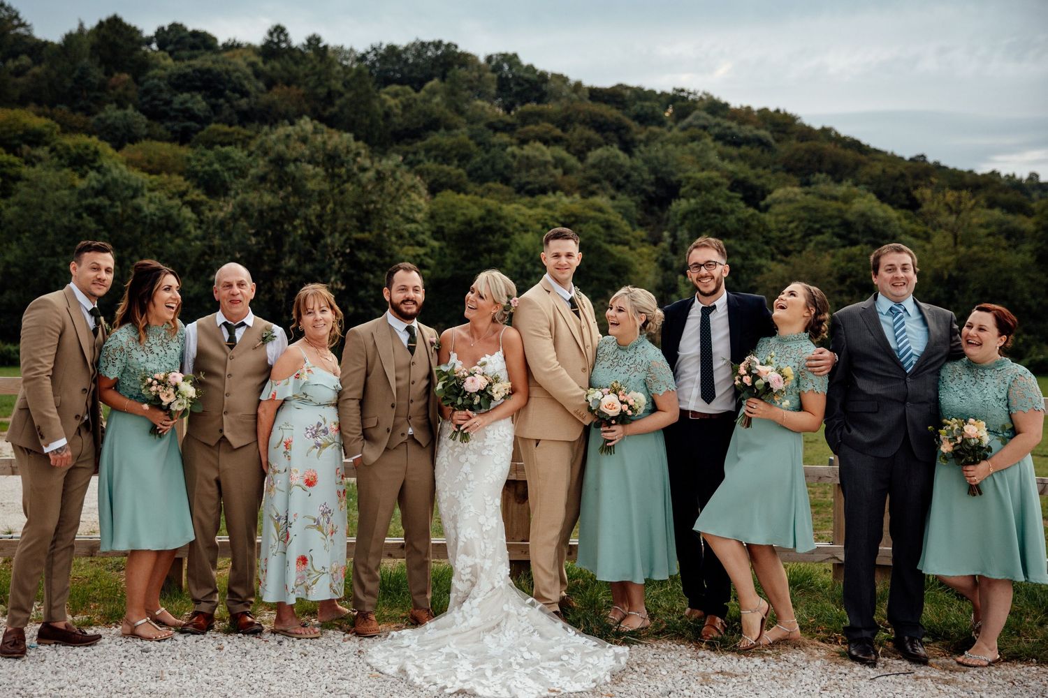 Wedding party in mint green dresses and brown suits posing outdoors on hillside.