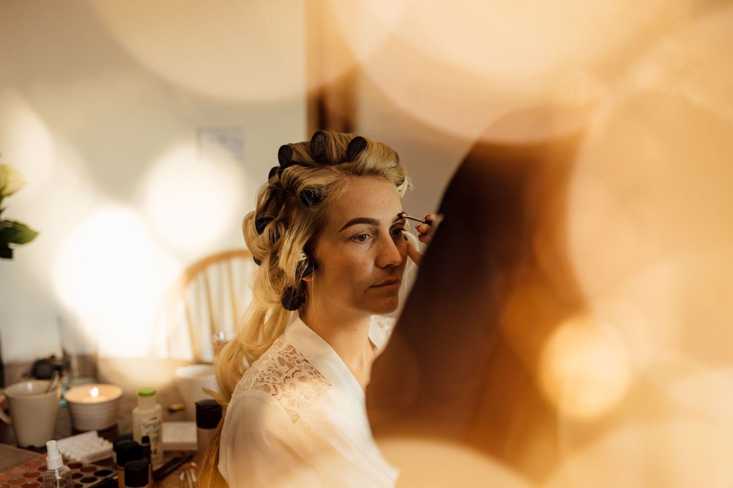 Soft focus wedding preparation scene with warm natural light streaming through window.
