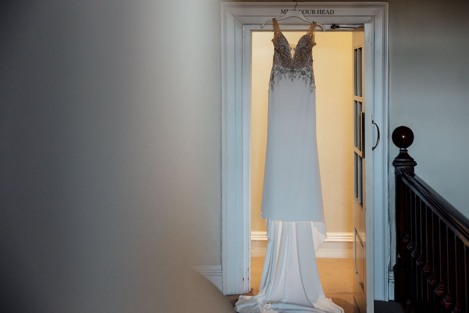 Elegant white wedding dress hanging in doorway with natural lighting.