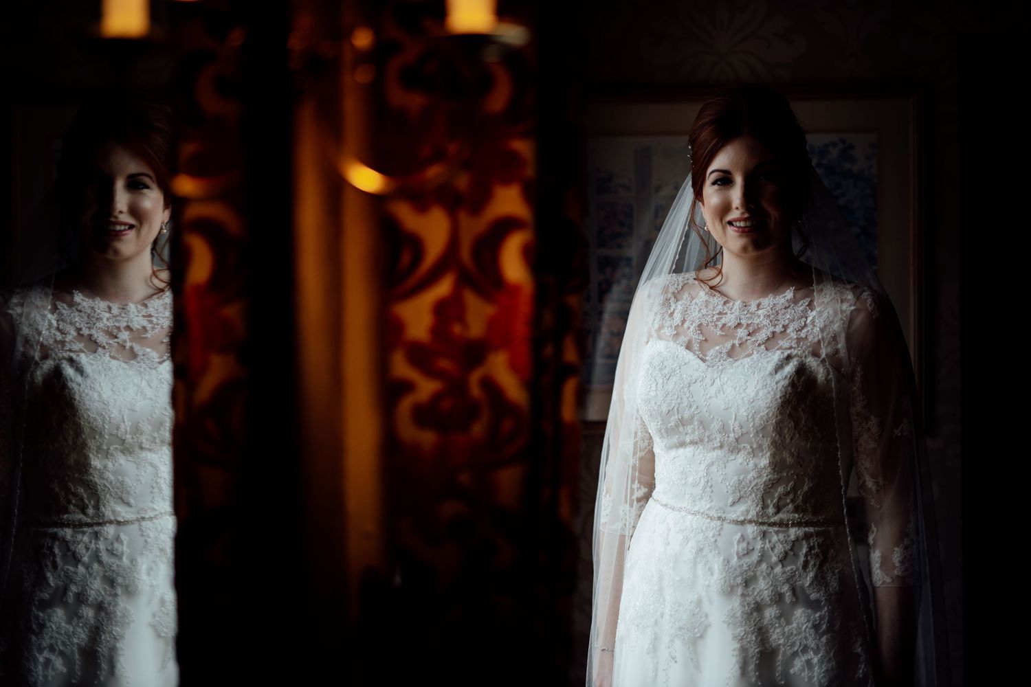Dramatic portrait of a bride in lace wedding dress with veil against dark moody lighting.