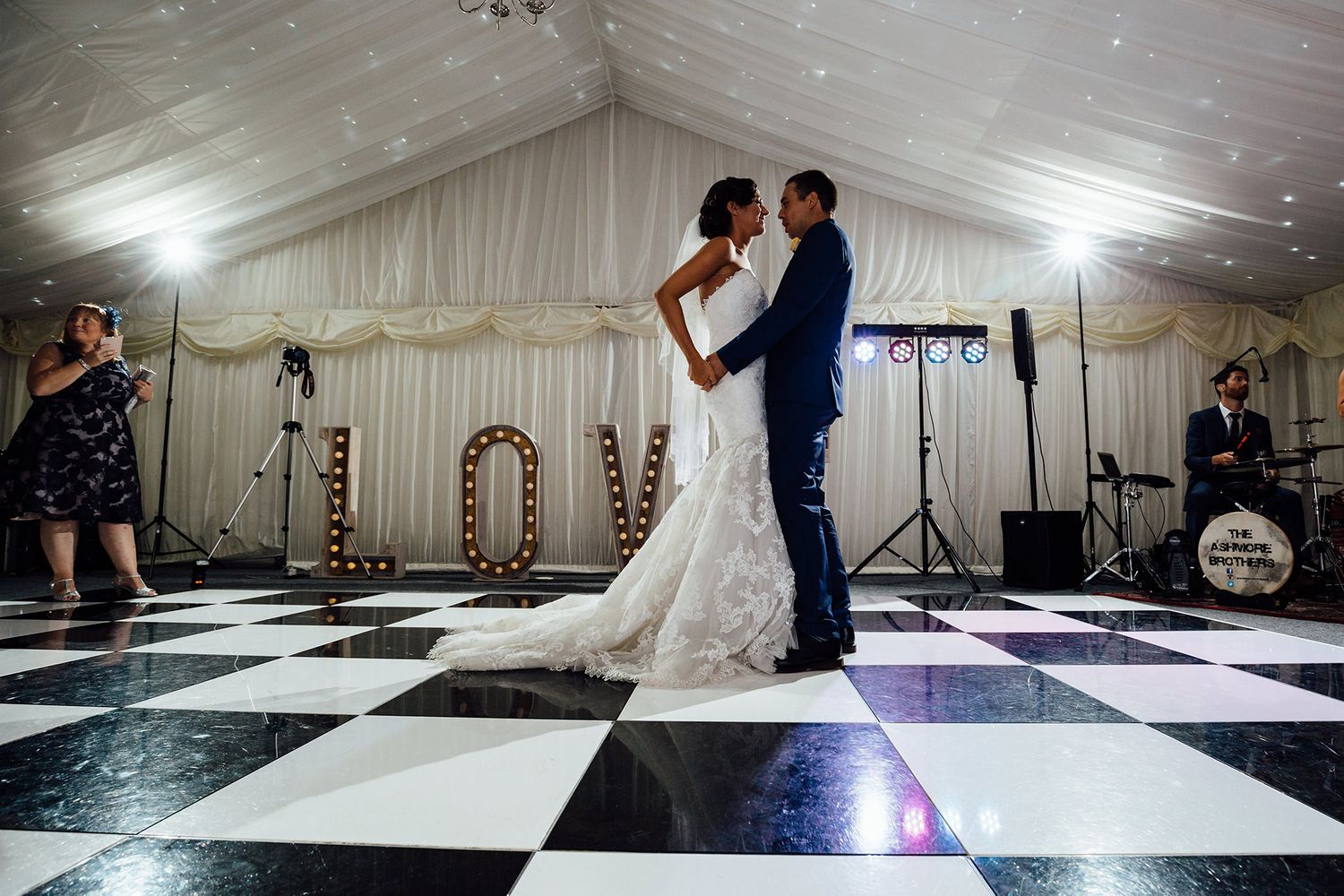 Wedding reception tent with black and white checkered dance floor and string lights.