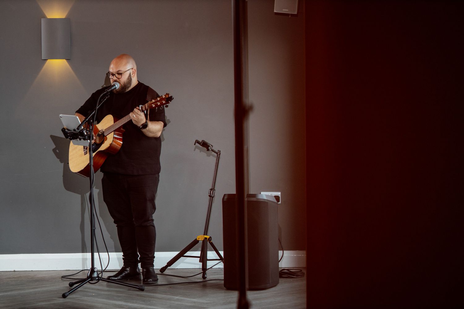 Musician performing in a dimly lit venue with acoustic guitar and microphone setup.