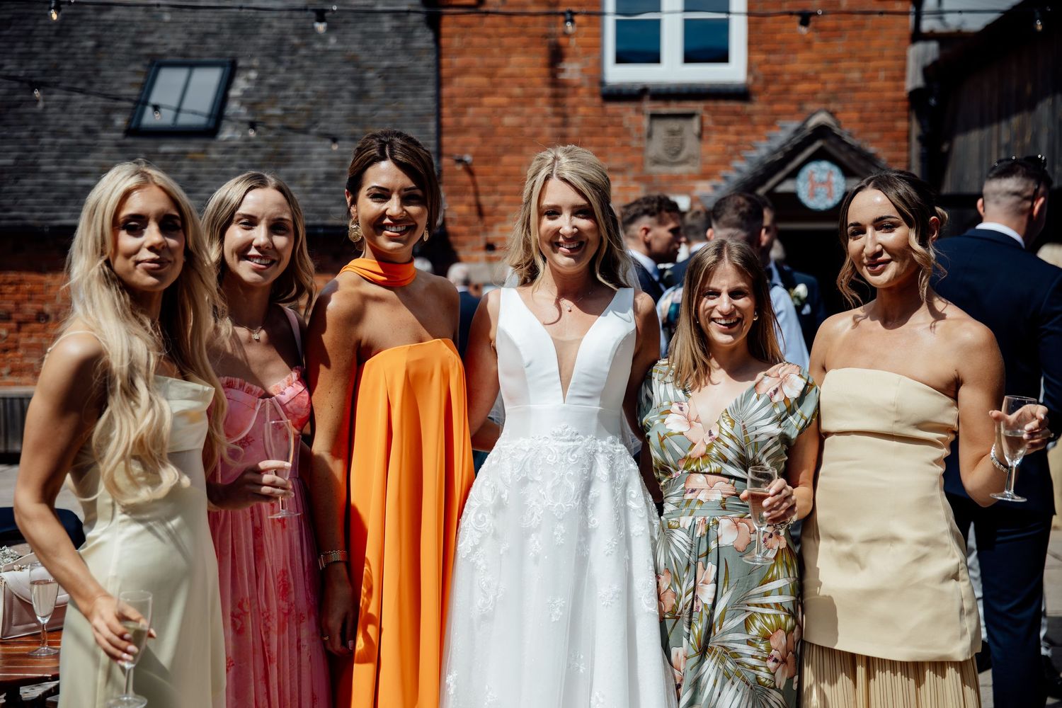Wedding party posing outdoors in front of red brick building wearing colorful attire.