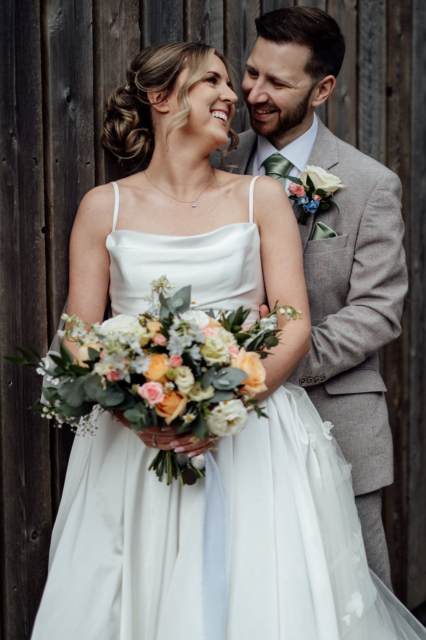 Intimate wedding portraits against rustic wooden barn backdrop with floral bouquets.