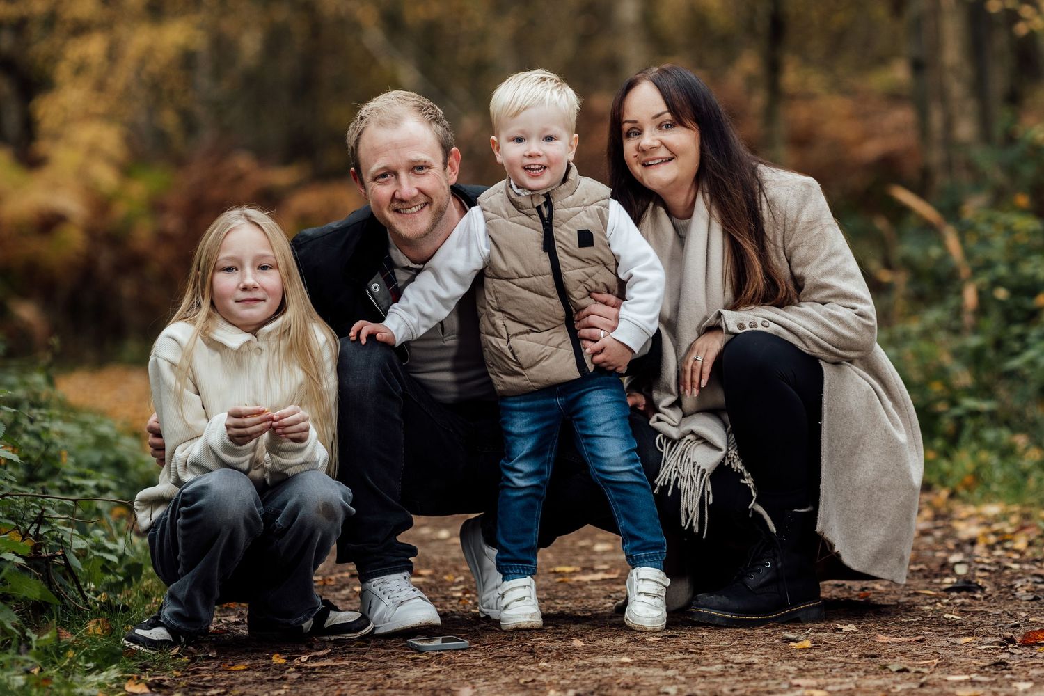 Family autumn portrait session with everyone sitting together on fallen leaves.