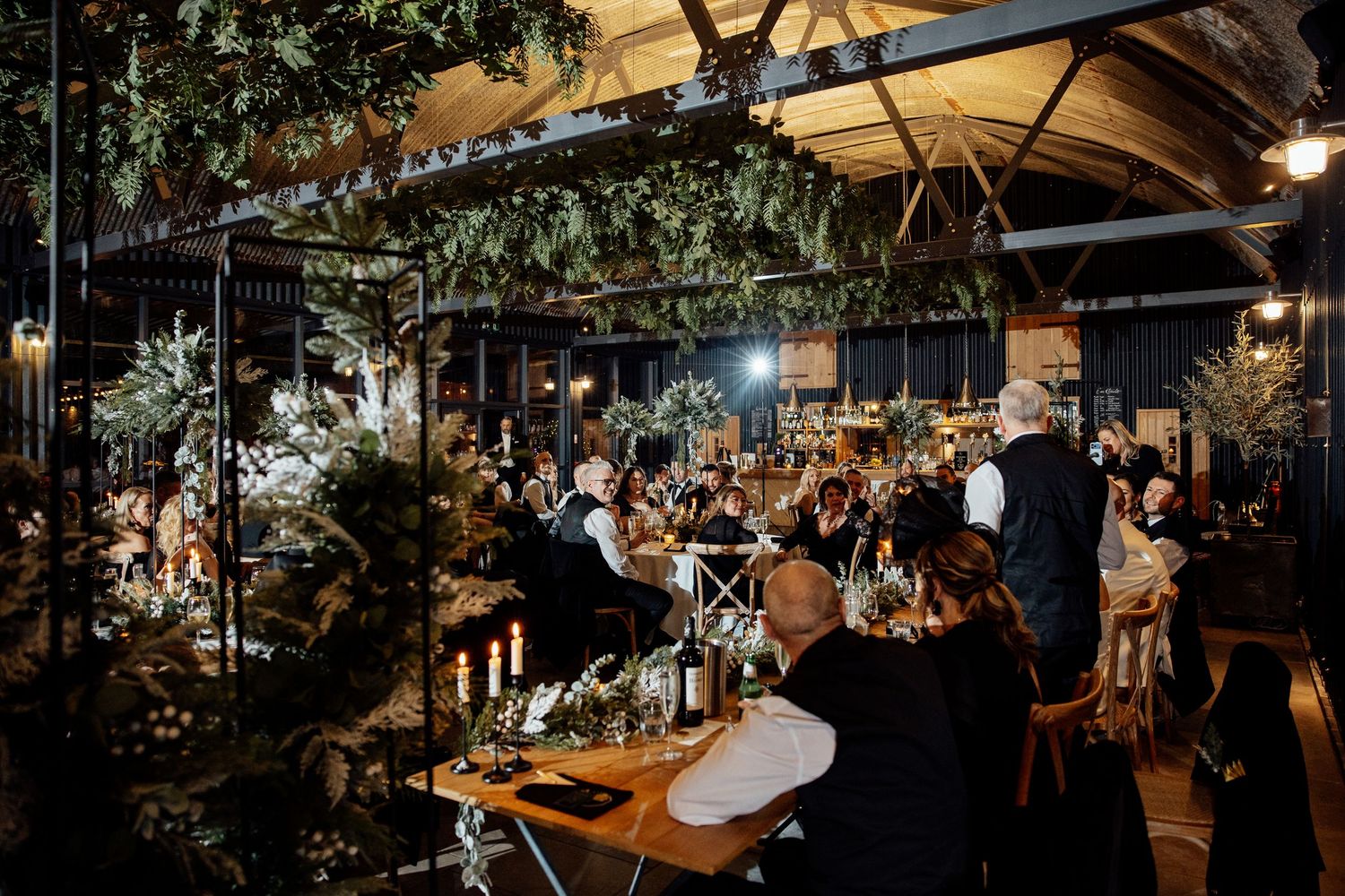 Wedding reception venue decorated with hanging greenery and ambient lighting creates an intimate atmosphere.