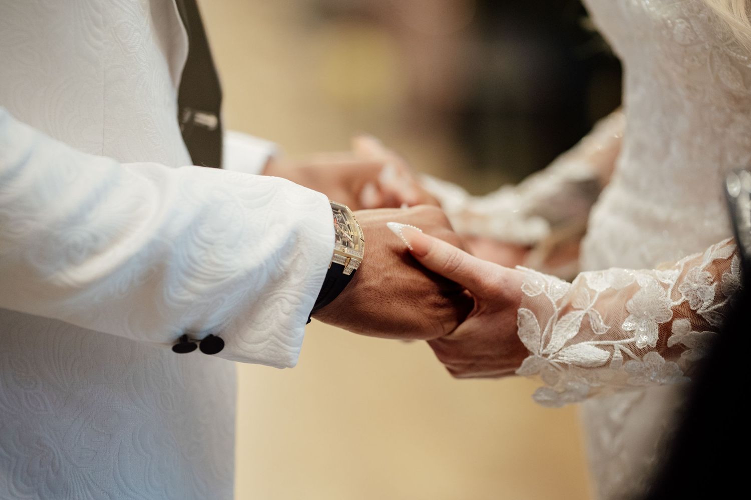 Close-up of bride and groom holding hands during wedding ring exchange ceremony.