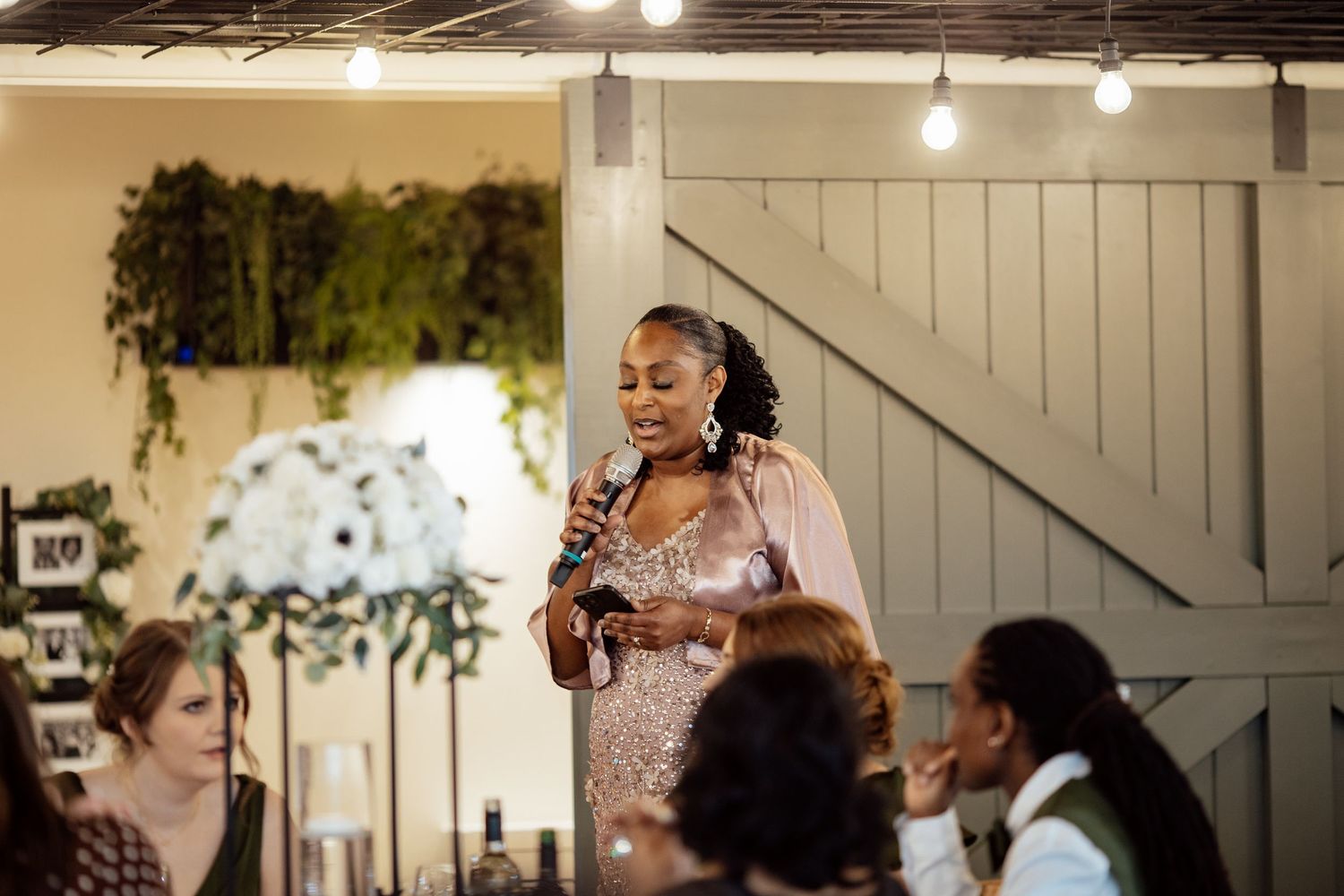 Elegant woman in sequin dress gives a heartfelt speech at a wedding reception with floral decor.