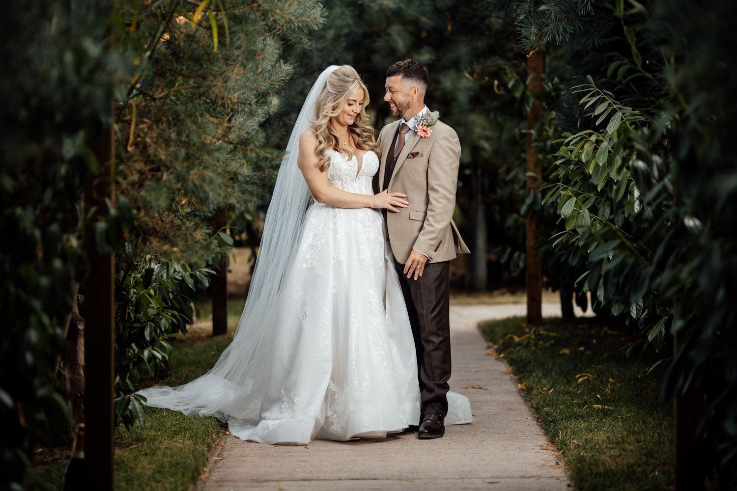 Bride and groom share a romantic moment on a garden pathway surrounded by lush greenery on their wedding day.
