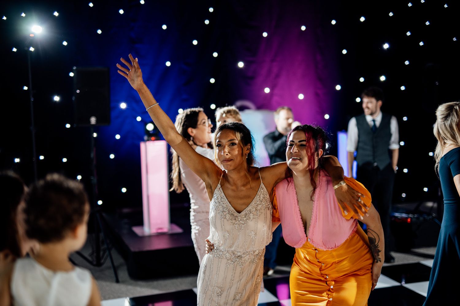 Guests dancing under colorful lights and starlit ceiling at wedding reception.