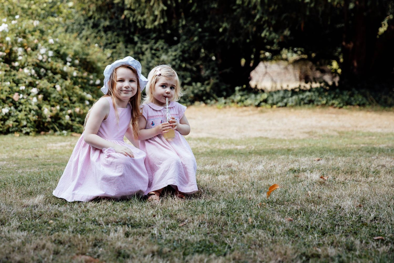 Mother and daughter in matching pink dresses laughing together on sunny lawn.