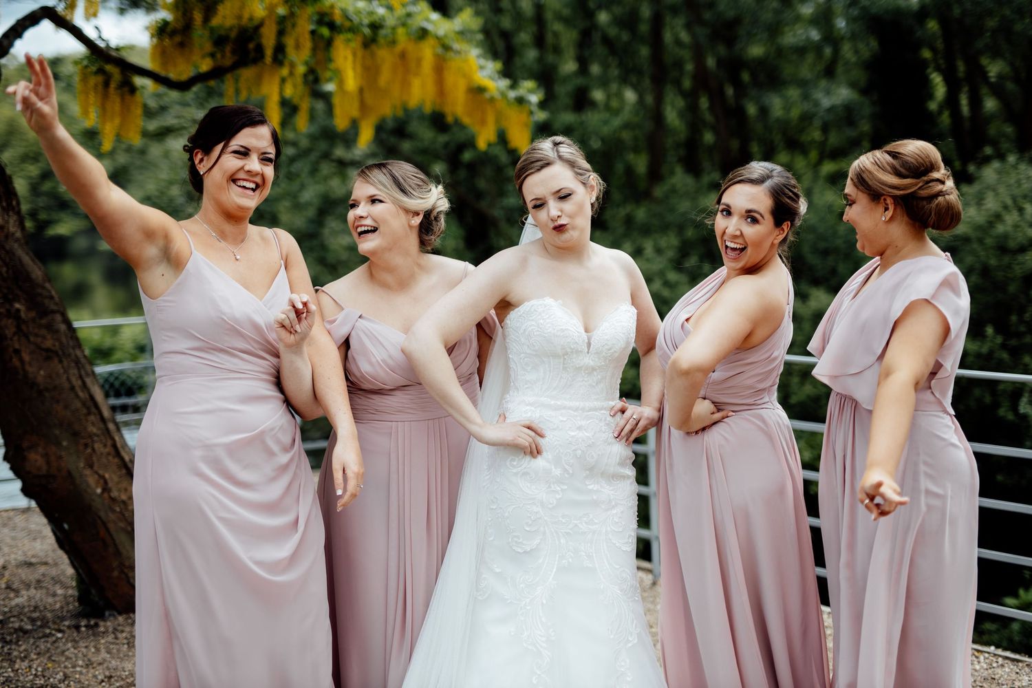 Bridal party in soft pink dresses shares joyful moment outdoors.