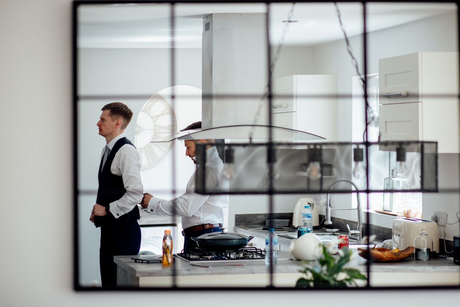 Chef in white vest working in professional kitchen reflected in mirror.