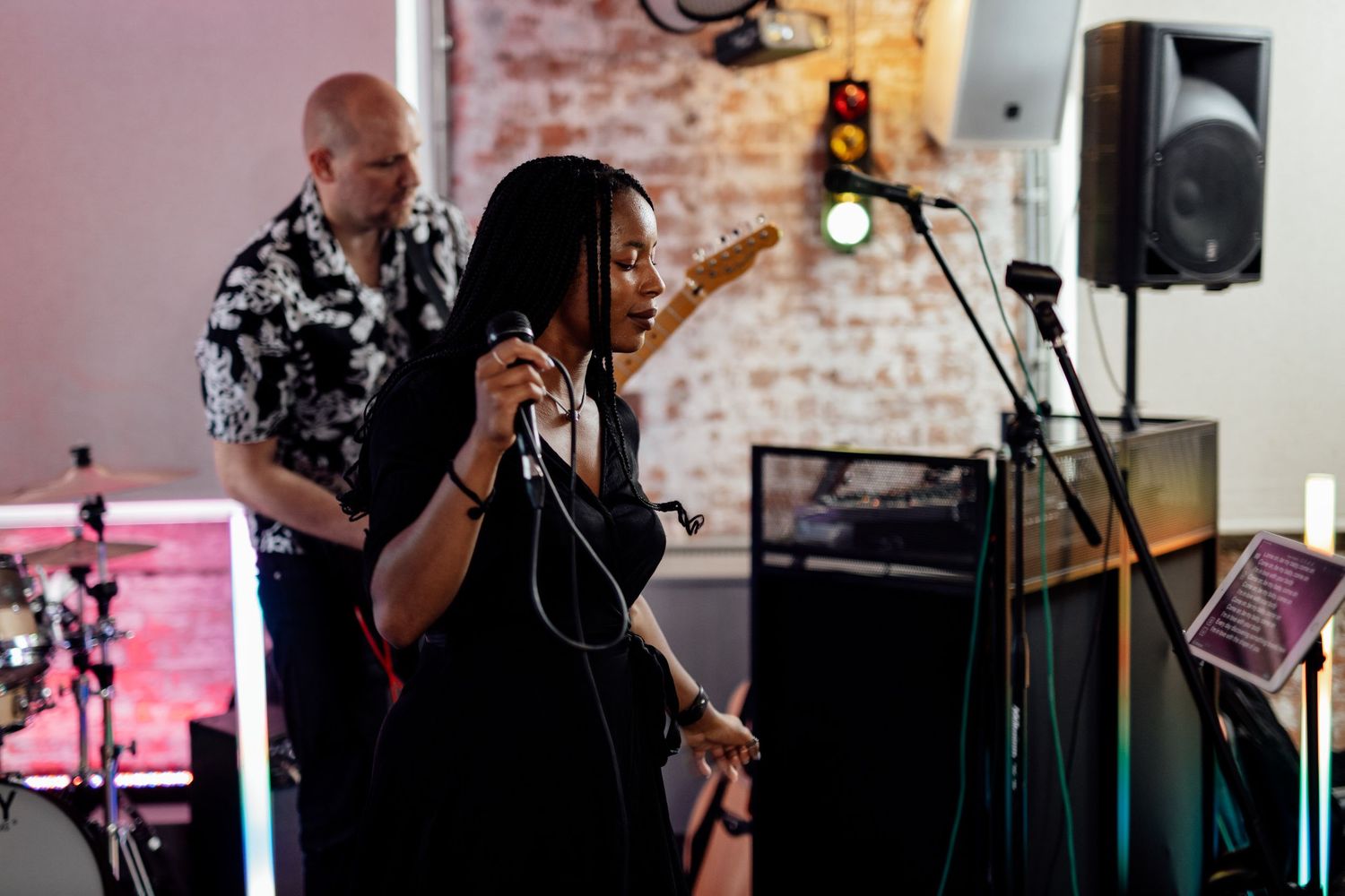 Band performs at wedding reception with singer at microphone against brick wall backdrop.