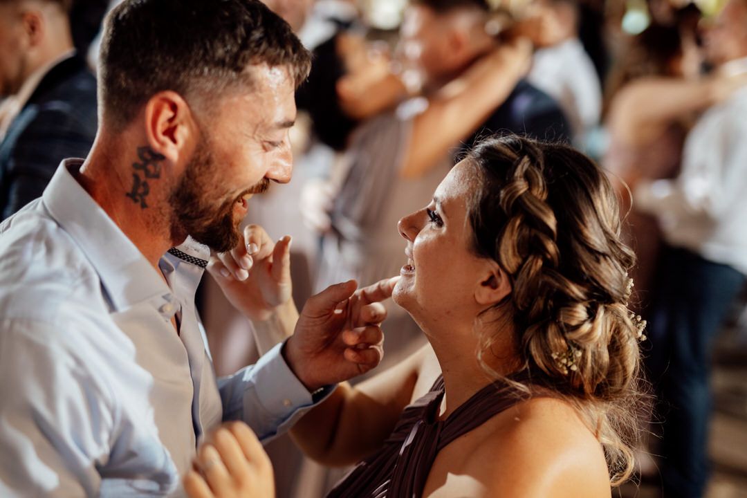 A couple shares a romantic dance moment at their wedding reception with warm lighting and guests in the background.