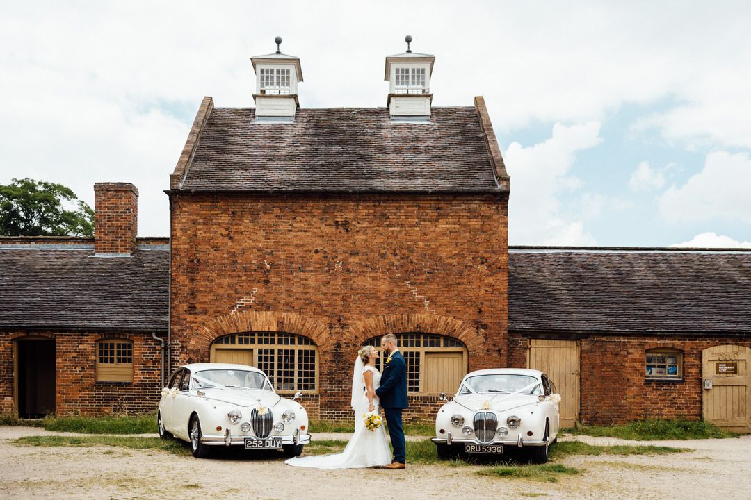 Classic wedding cars parked outside traditional brick building venue.