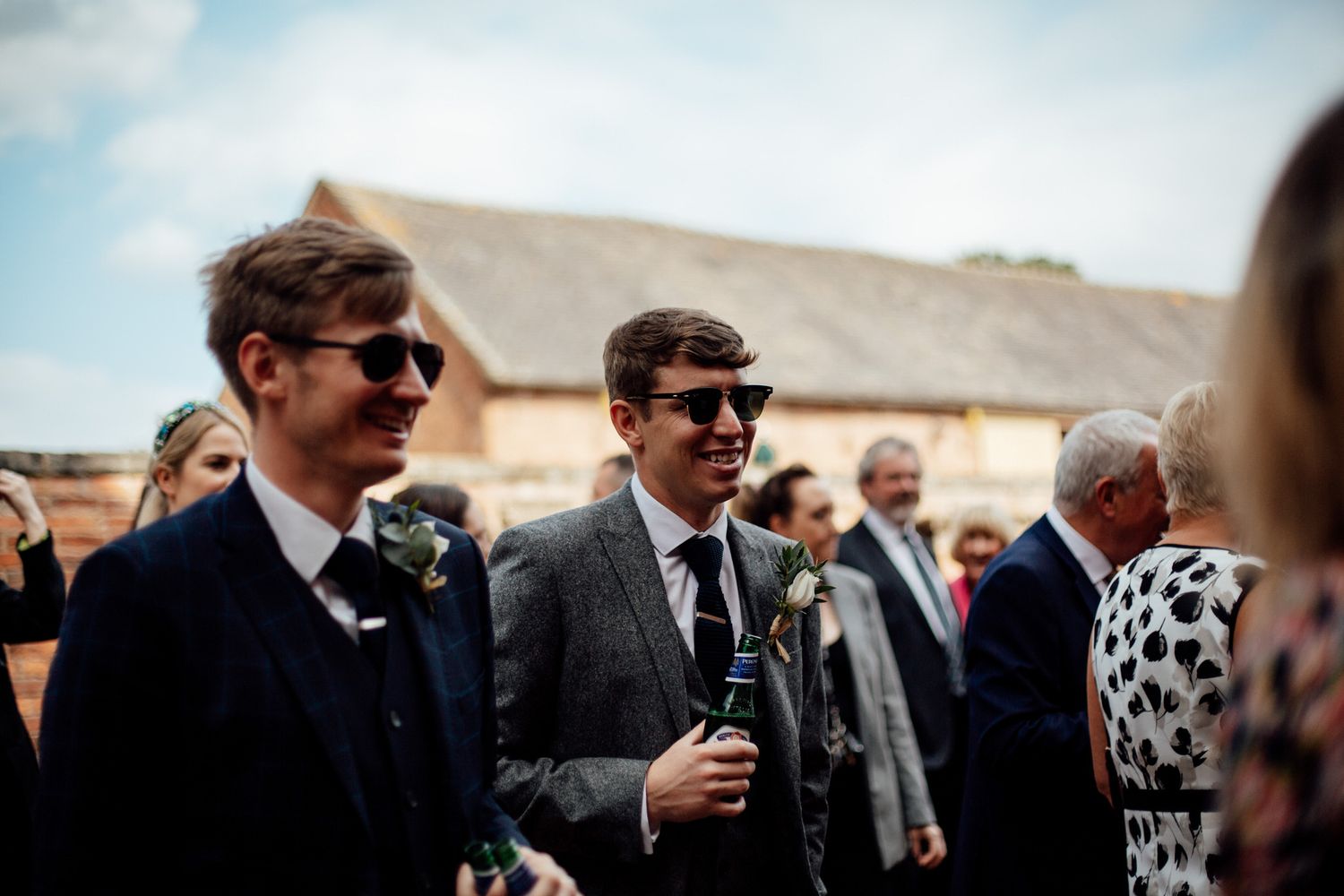 Wedding guests in sunglasses enjoying drinks at outdoor reception.