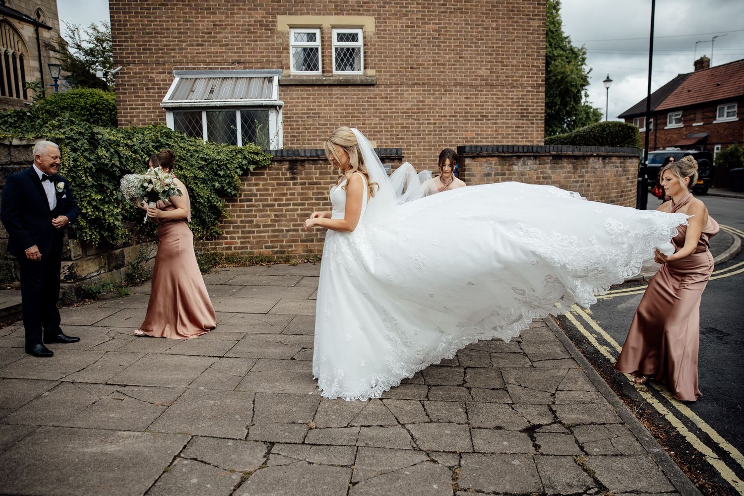 Wedding party walks along stone pathway outside brick building.