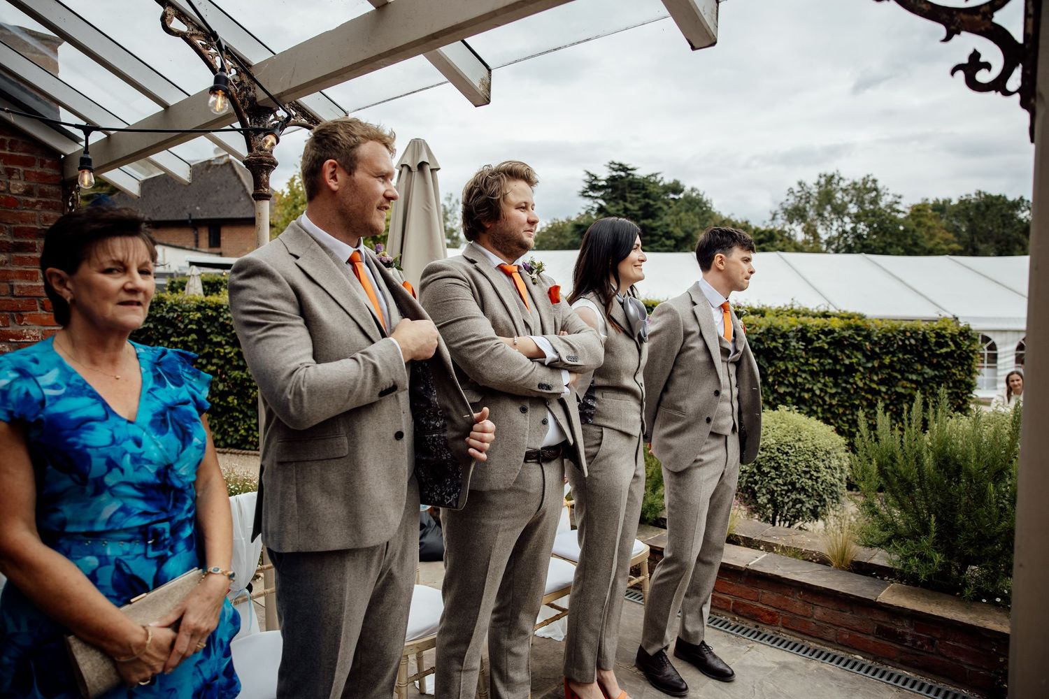 Wedding party in gray suits and blue dresses stand together during an outdoor celebration.