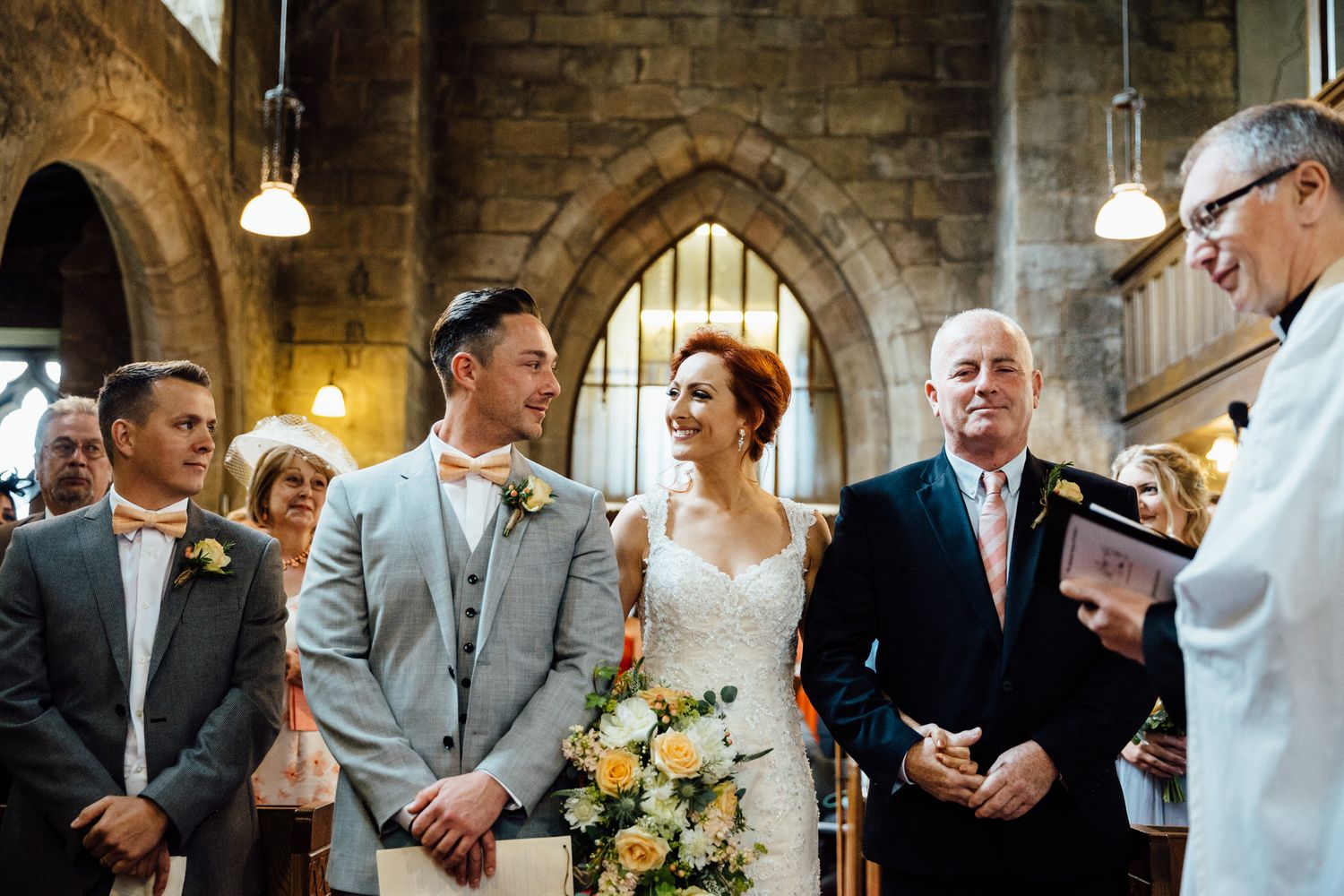 Wedding ceremony taking place inside historic stone church with arched architecture.