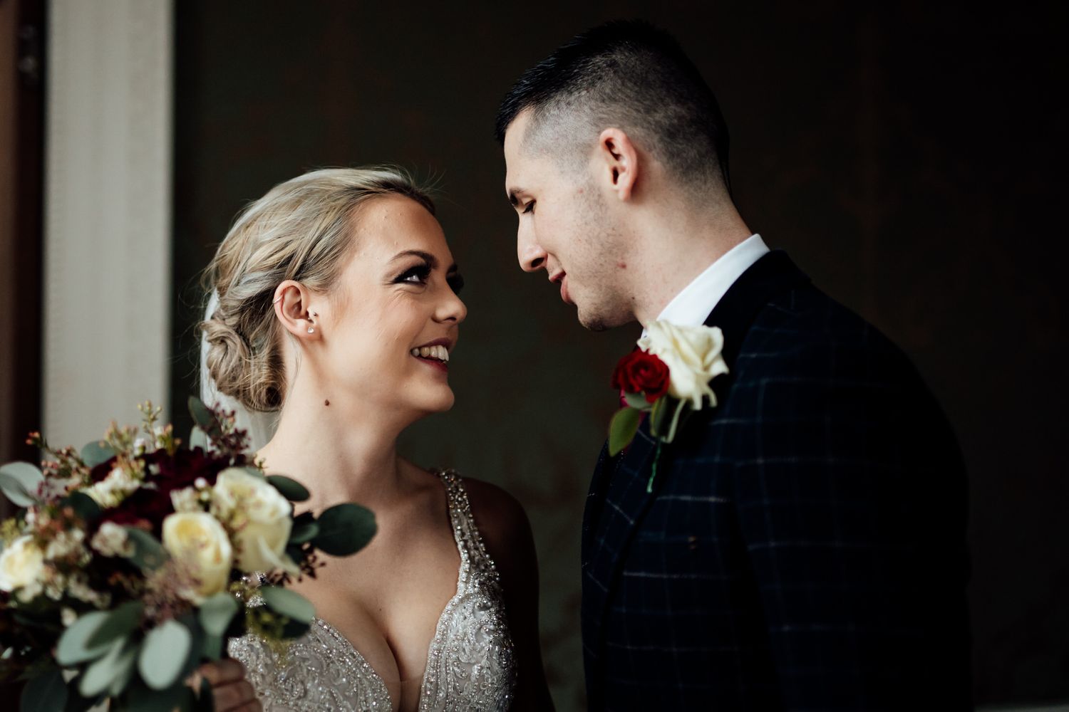 Romantic wedding portrait captured in dramatic lighting against dark background.