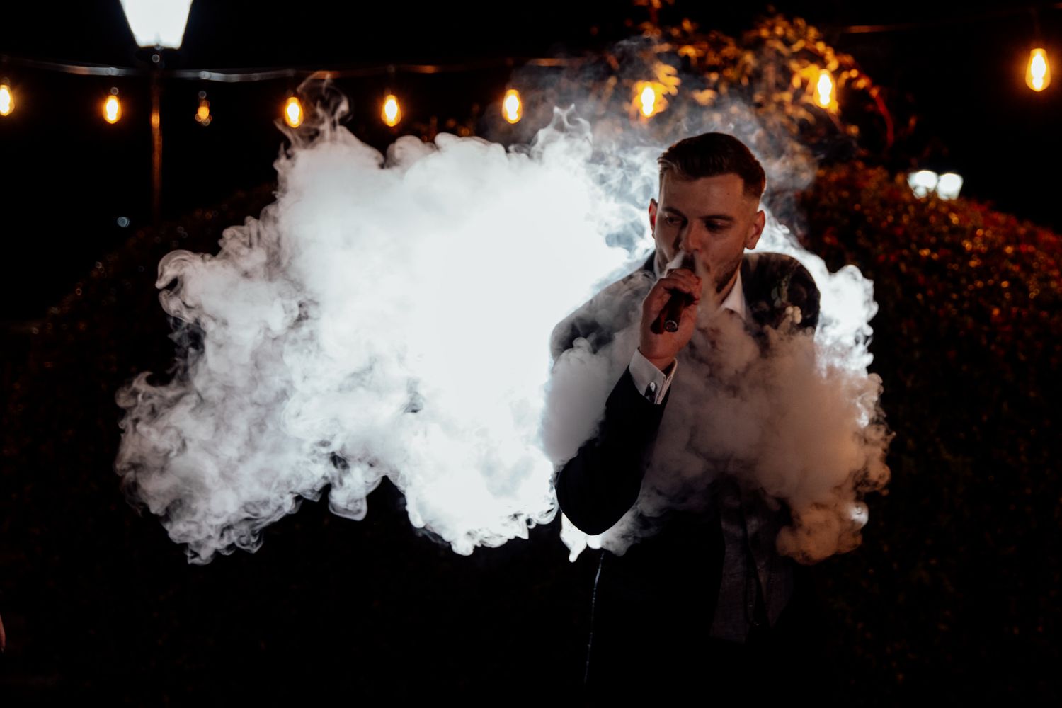 White smoke creates dramatic effect during evening wedding celebration with string lights.