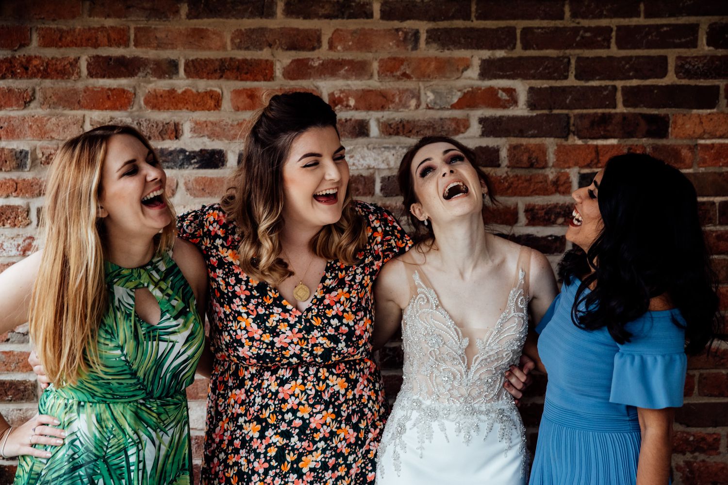 Wedding party sharing laughs against rustic brick wall backdrop.