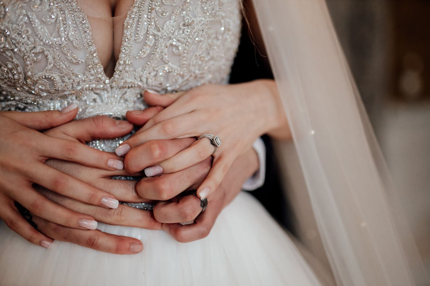 Close-up details of hands and wedding rings against a beaded dress background.