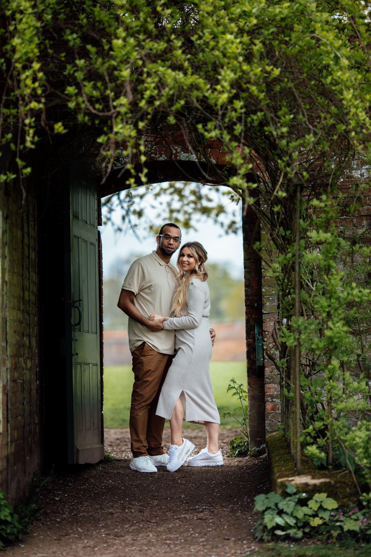 A couple embraces in a lush green archway of foliage during an outdoor photoshoot.