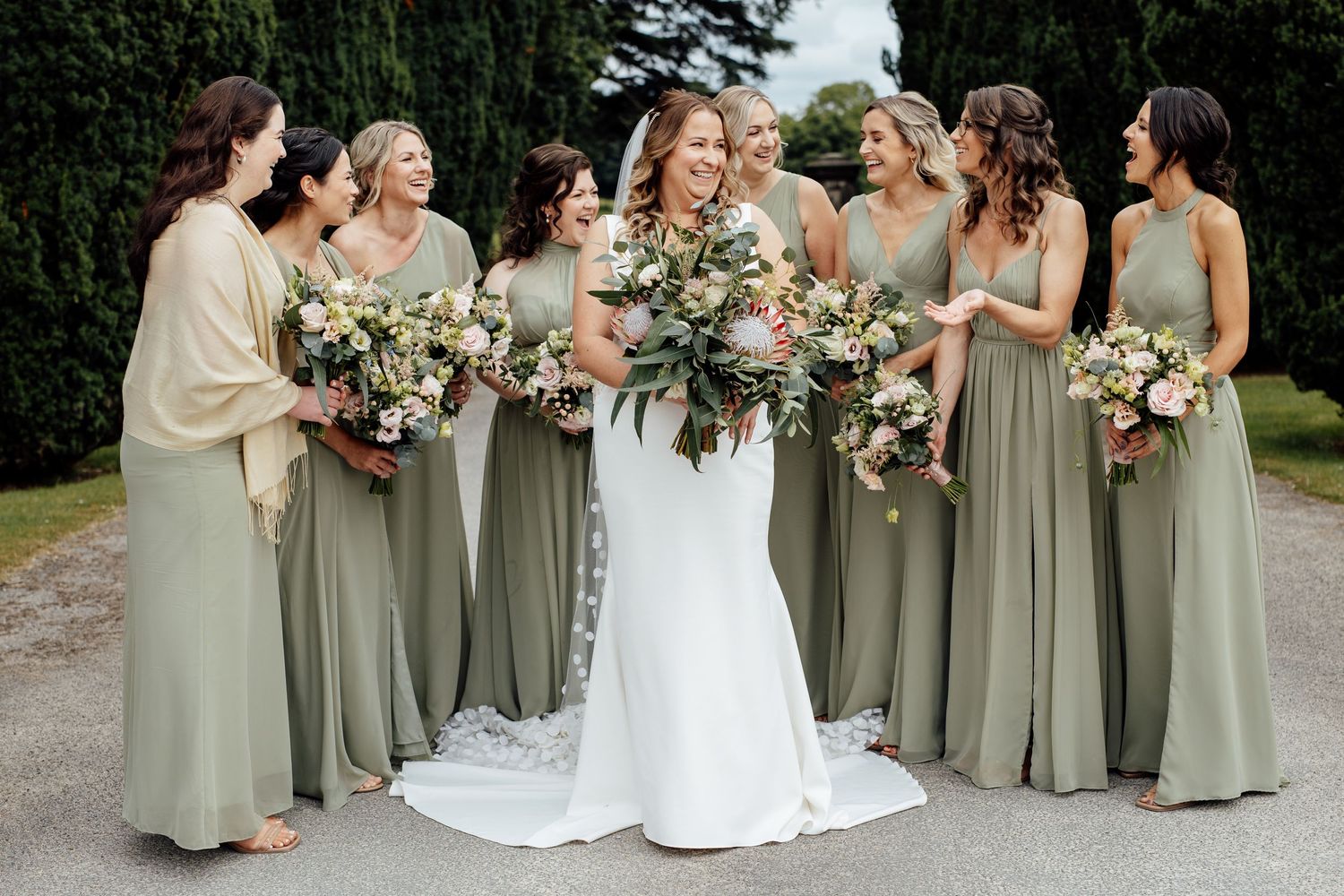 Bridal party in sage green dresses posing with bouquets for formal photos.