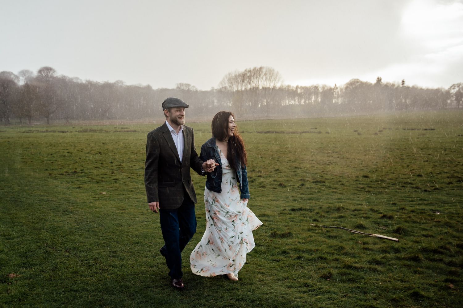 A couple poses playfully in an open field during golden hour.