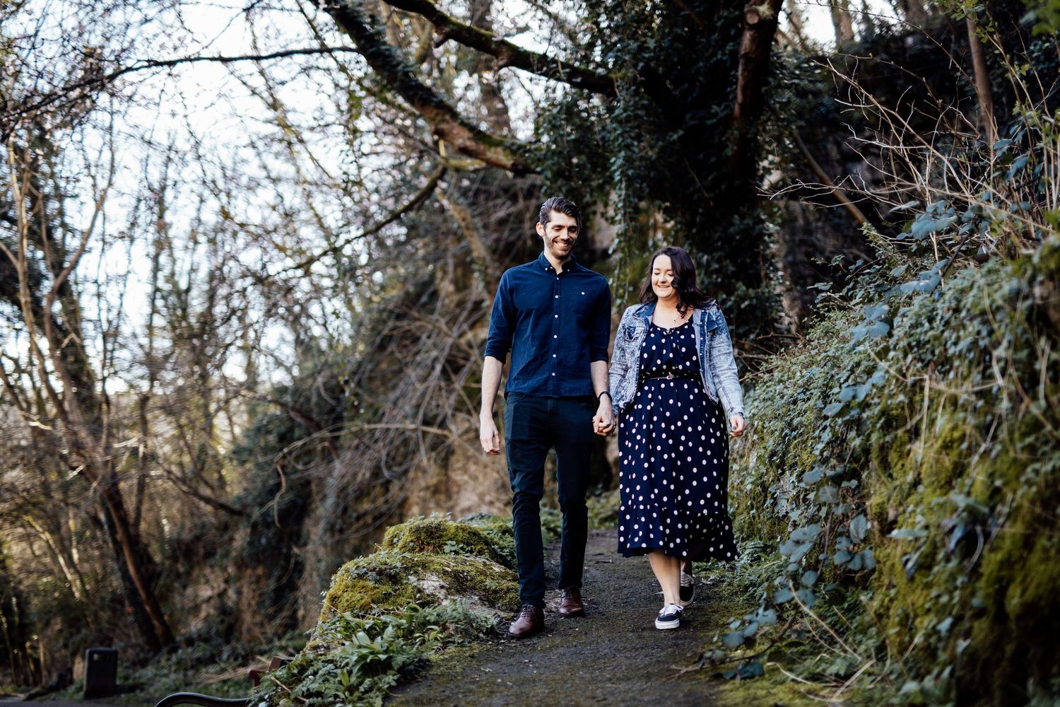 Two people enjoy a peaceful walk through a wooded park trail.