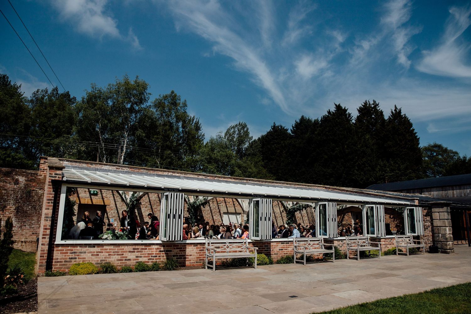 Long modern venue building exterior with large windows under bright blue summer sky.