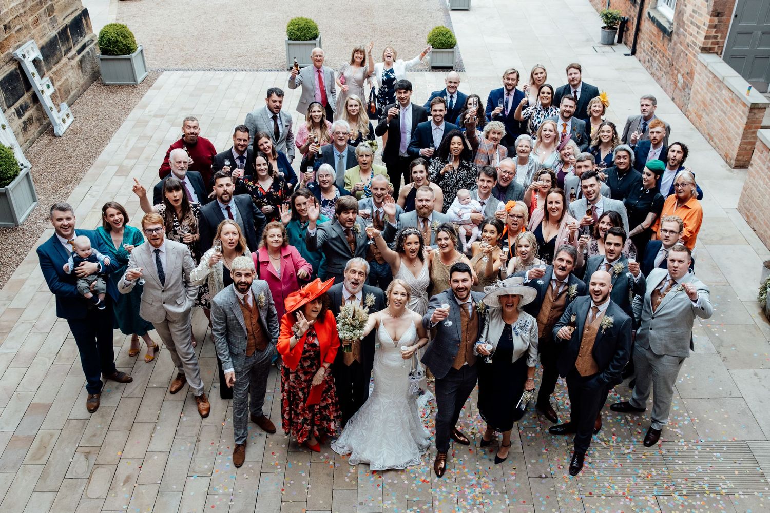 Aerial view of large wedding party group photo outside brick building.