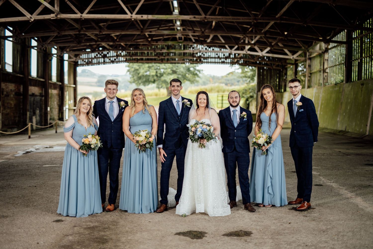 Wedding party poses for group photo in rustic industrial venue setting.