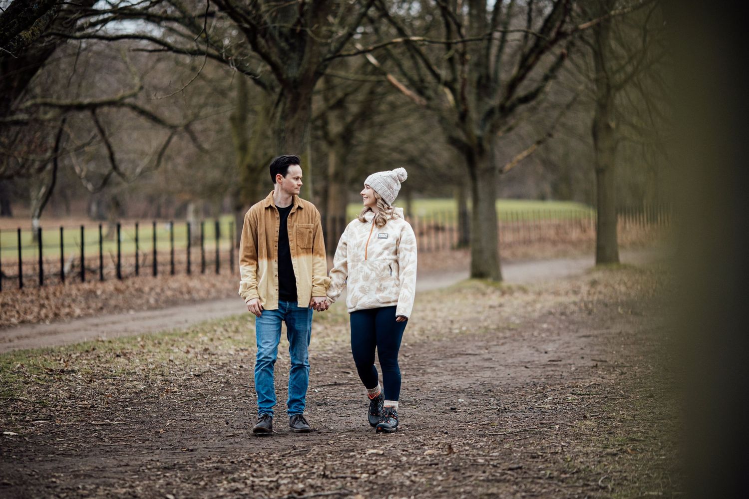 Couple enjoying a playful moment together on a path surrounded by bare winter trees.