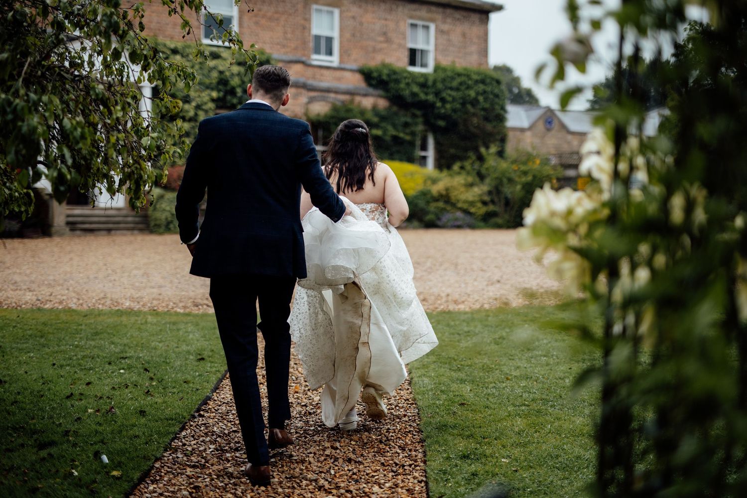 Wedding couple walking through garden path surrounded by greenery.