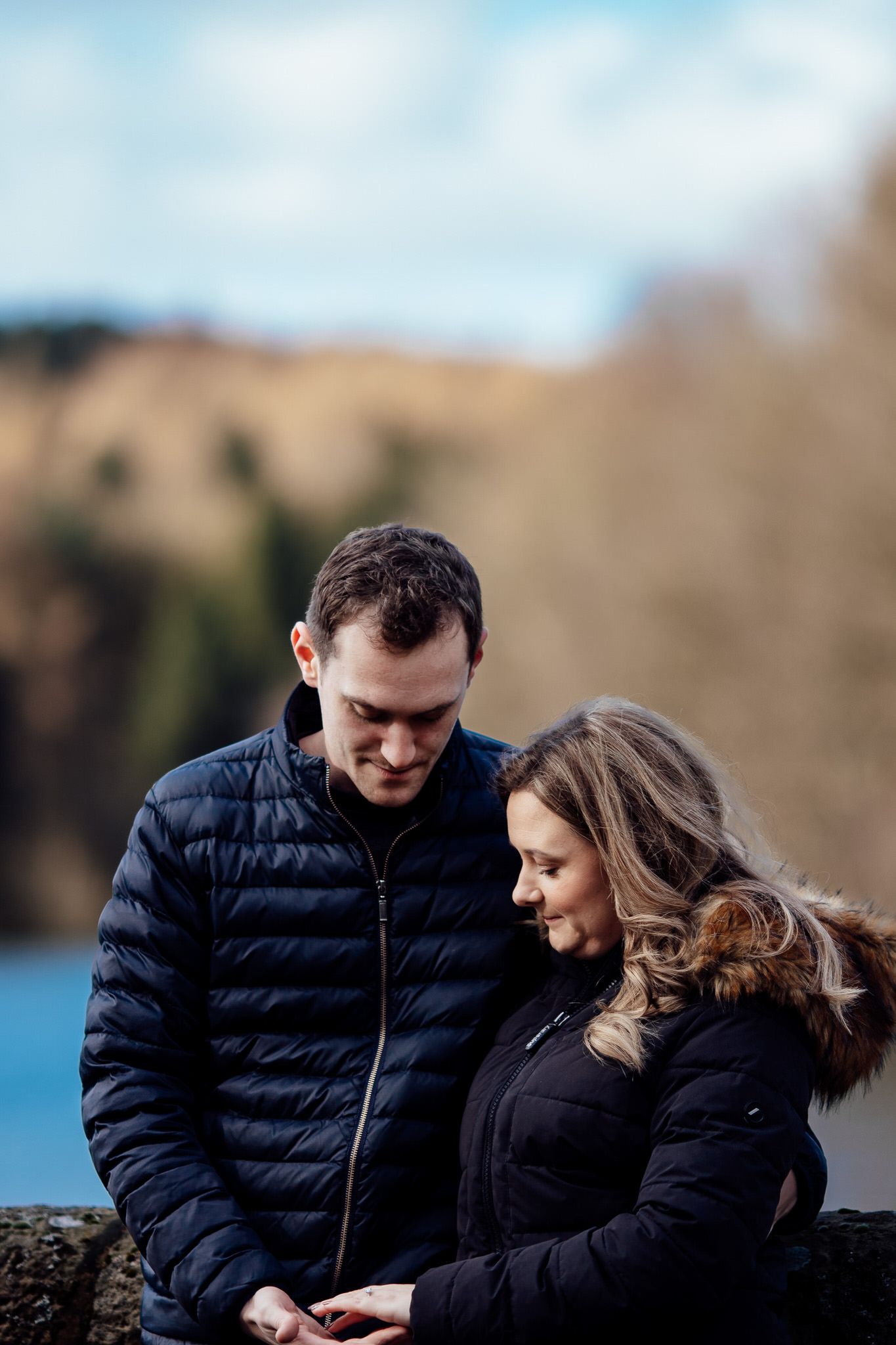 Couple in matching black puffer jackets sharing tender moments by waterfront.