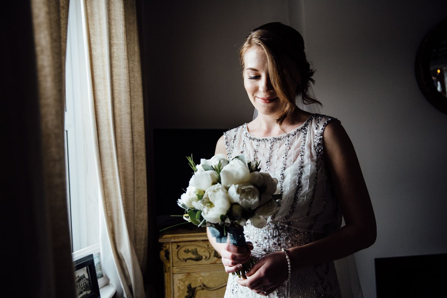 Elegant bridal preparations captured in dramatic window lighting.