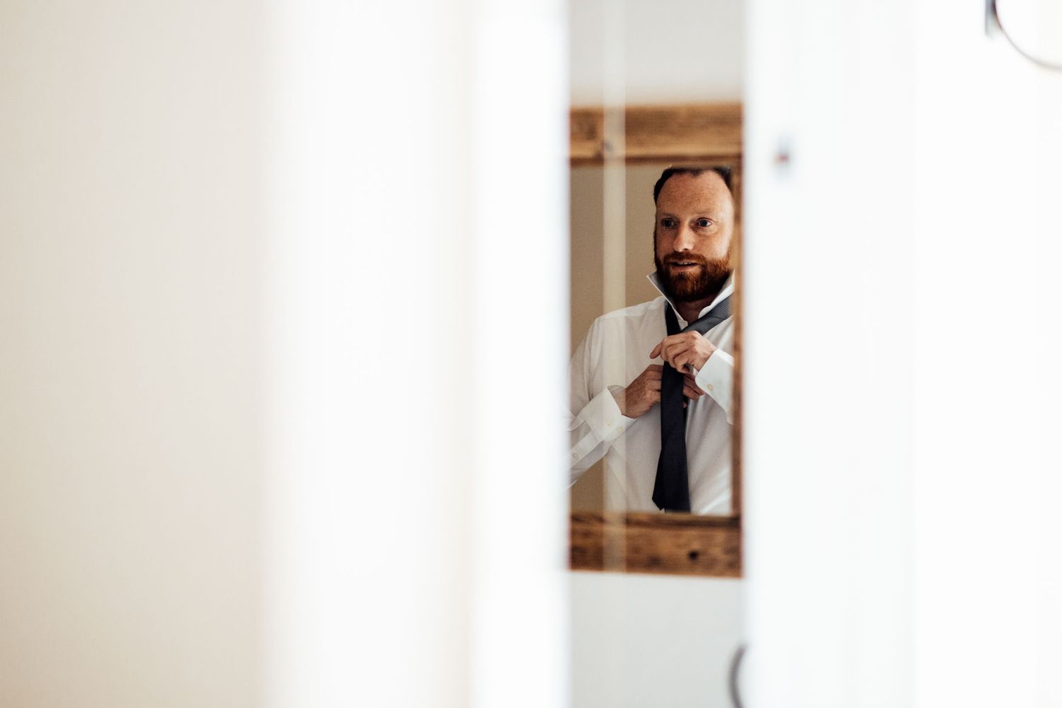 Candid wedding preparation moments captured through doorways and windows.