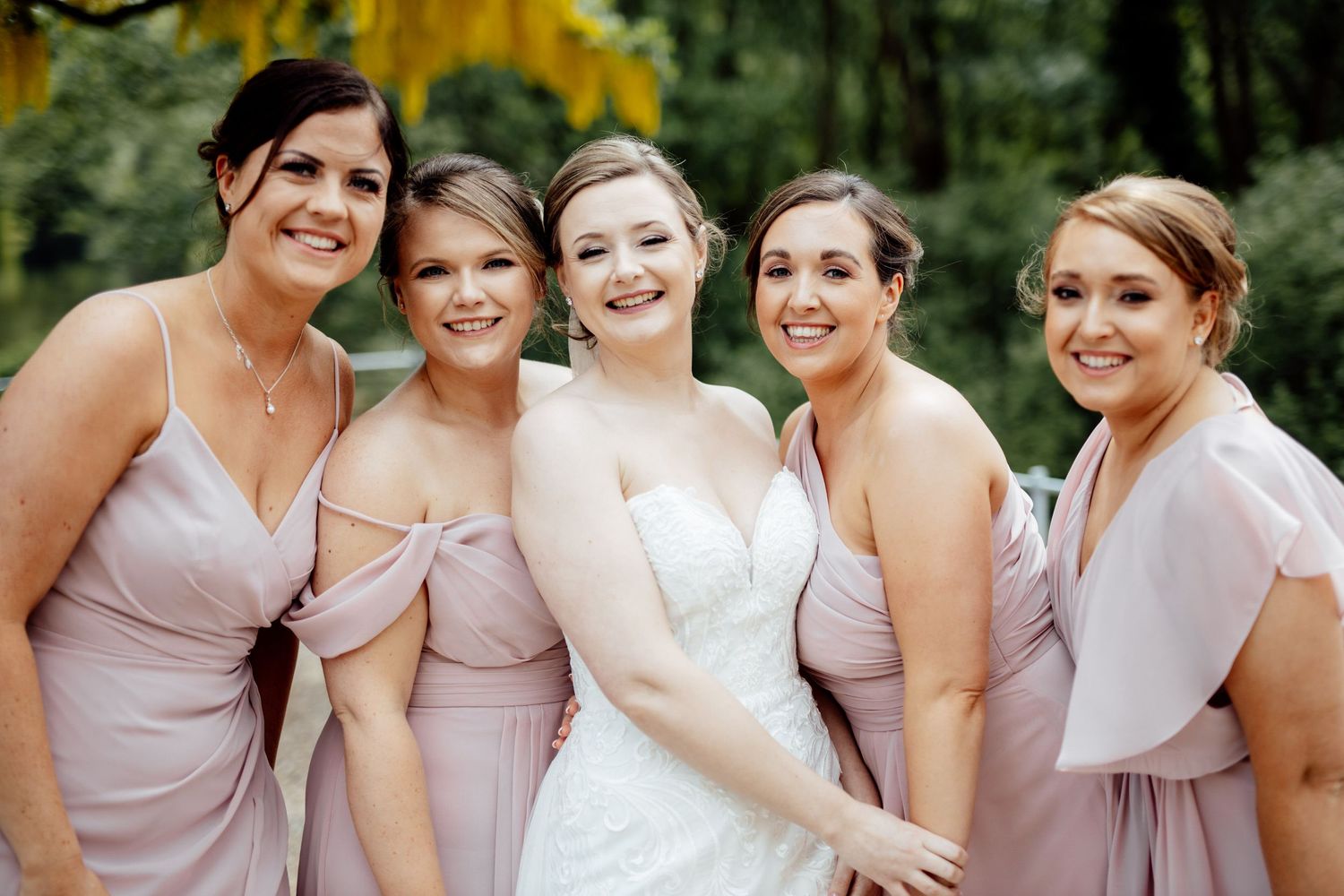 Bridesmaids in light pink dresses pose together outdoors.