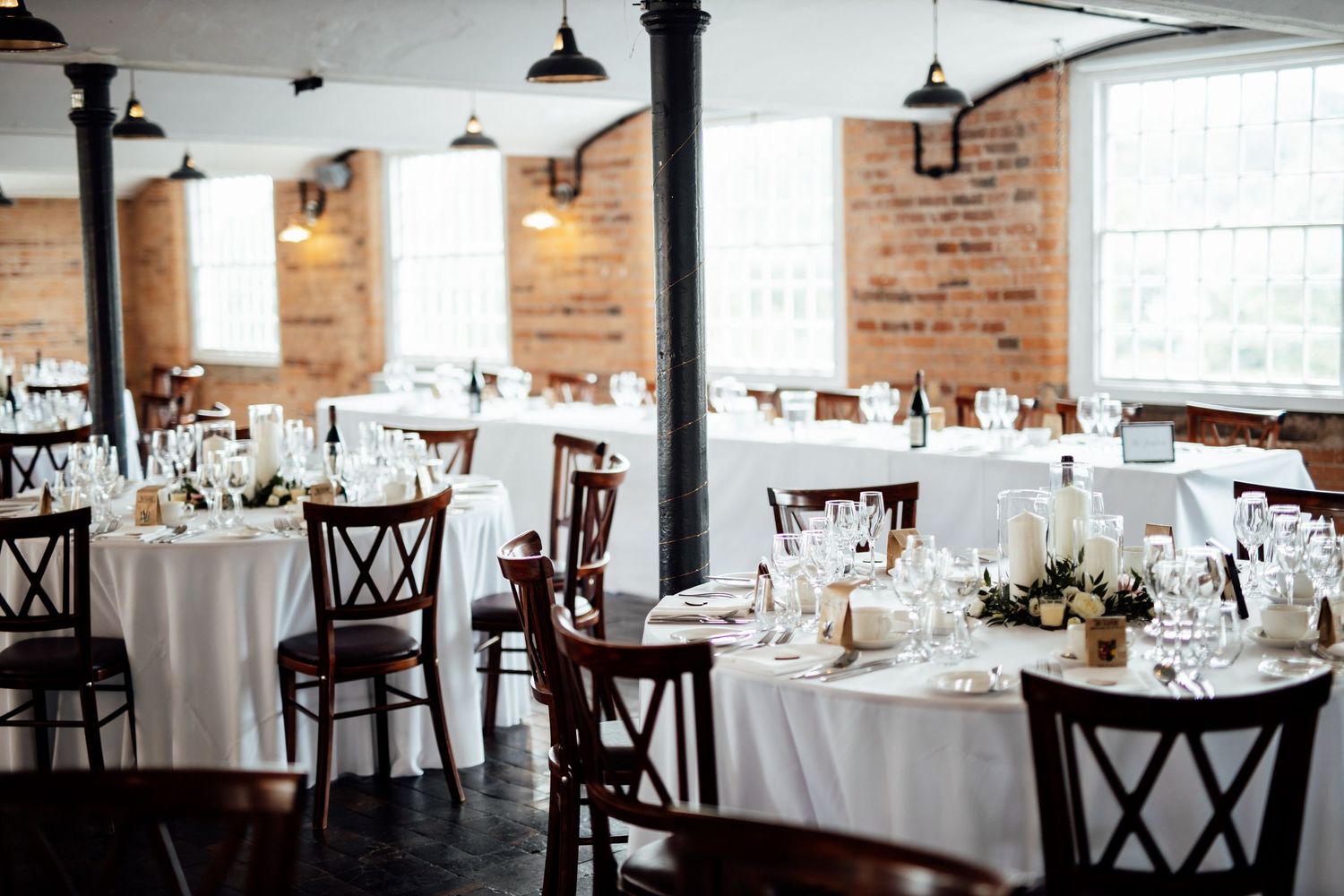 Empty wedding reception venue with white tablecloths and exposed brick walls.