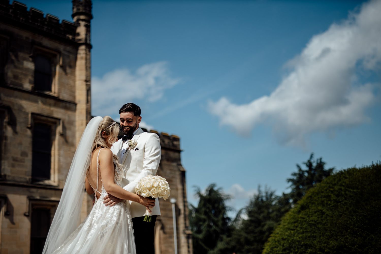 Wedding couple shares intimate moment against historic stone architecture on sunny day.
