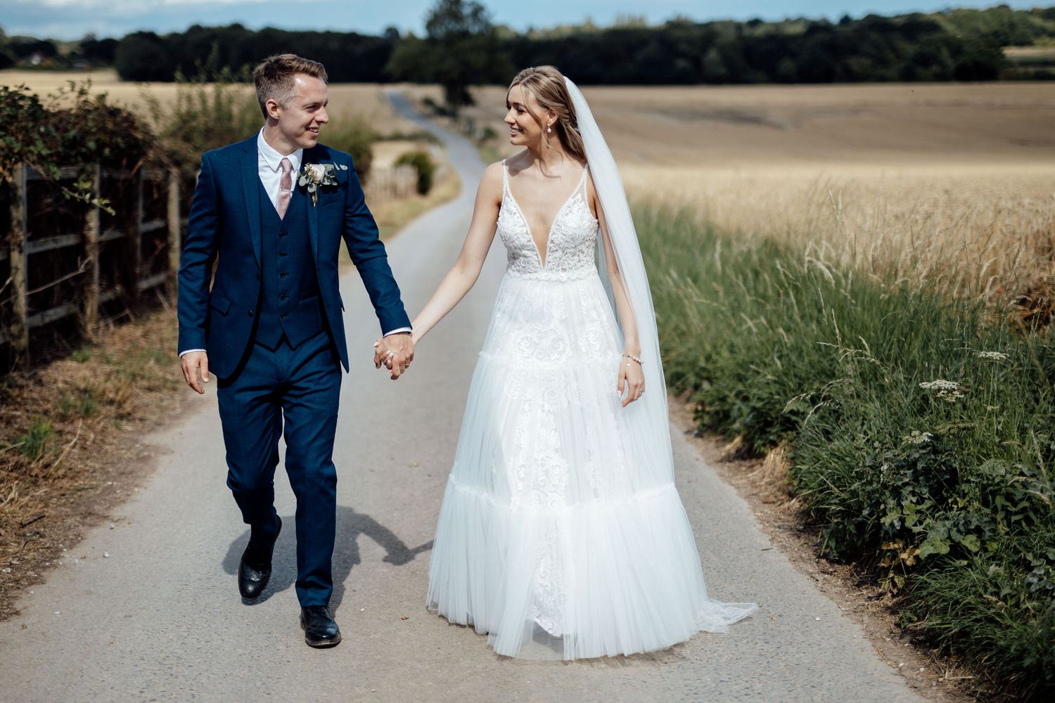 A couple strolls hand in hand along a country path on their wedding day.