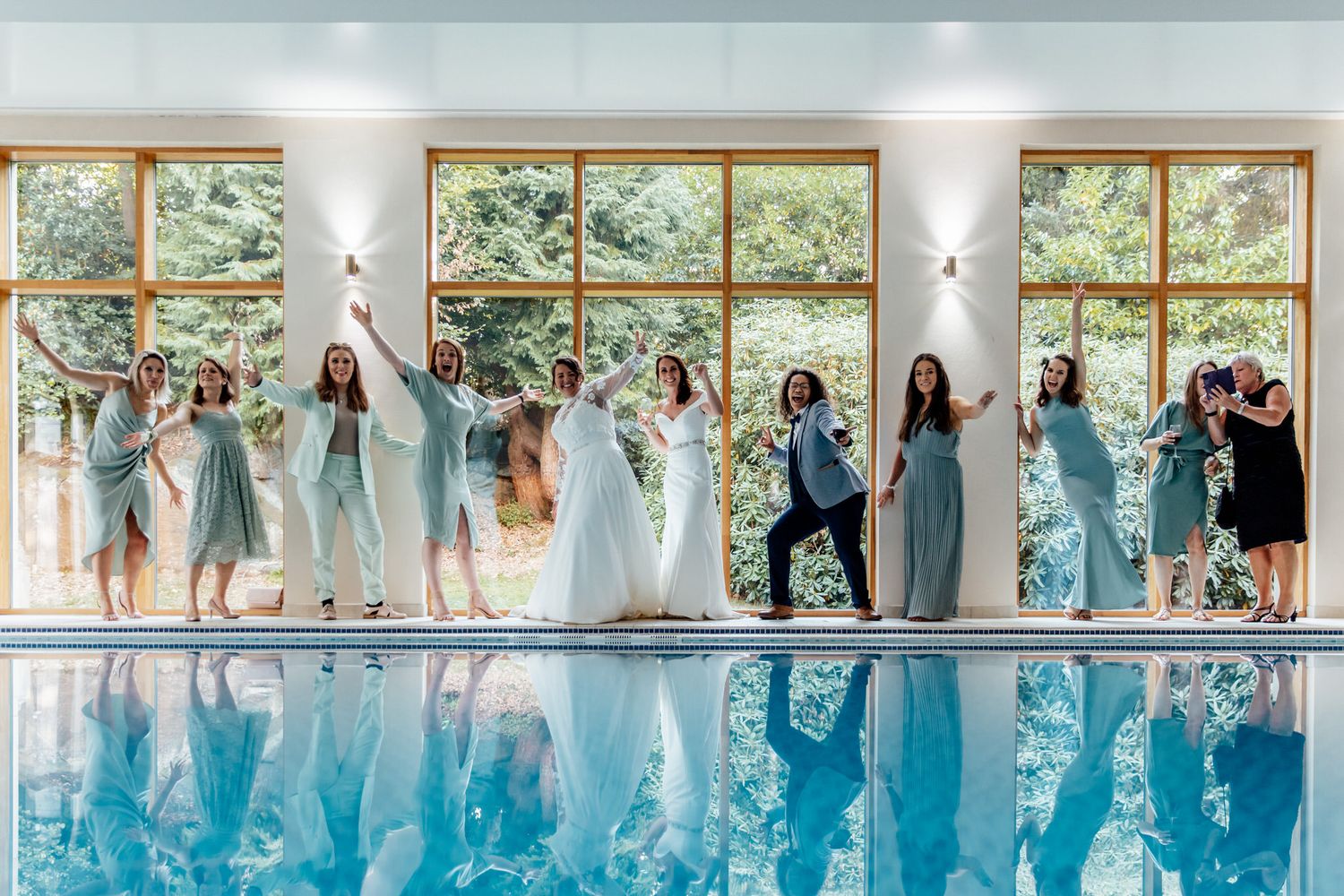 Wedding party poses in front of large windows in light blue and formal attire.
