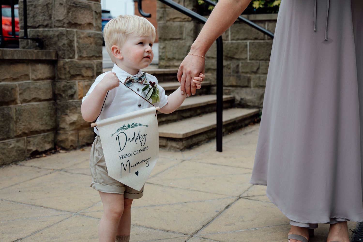Young ring bearer in formal attire walking among wedding guests in gray dresses.