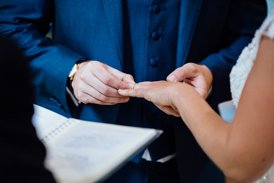 Close-up of hands exchanging wedding rings during ceremony.