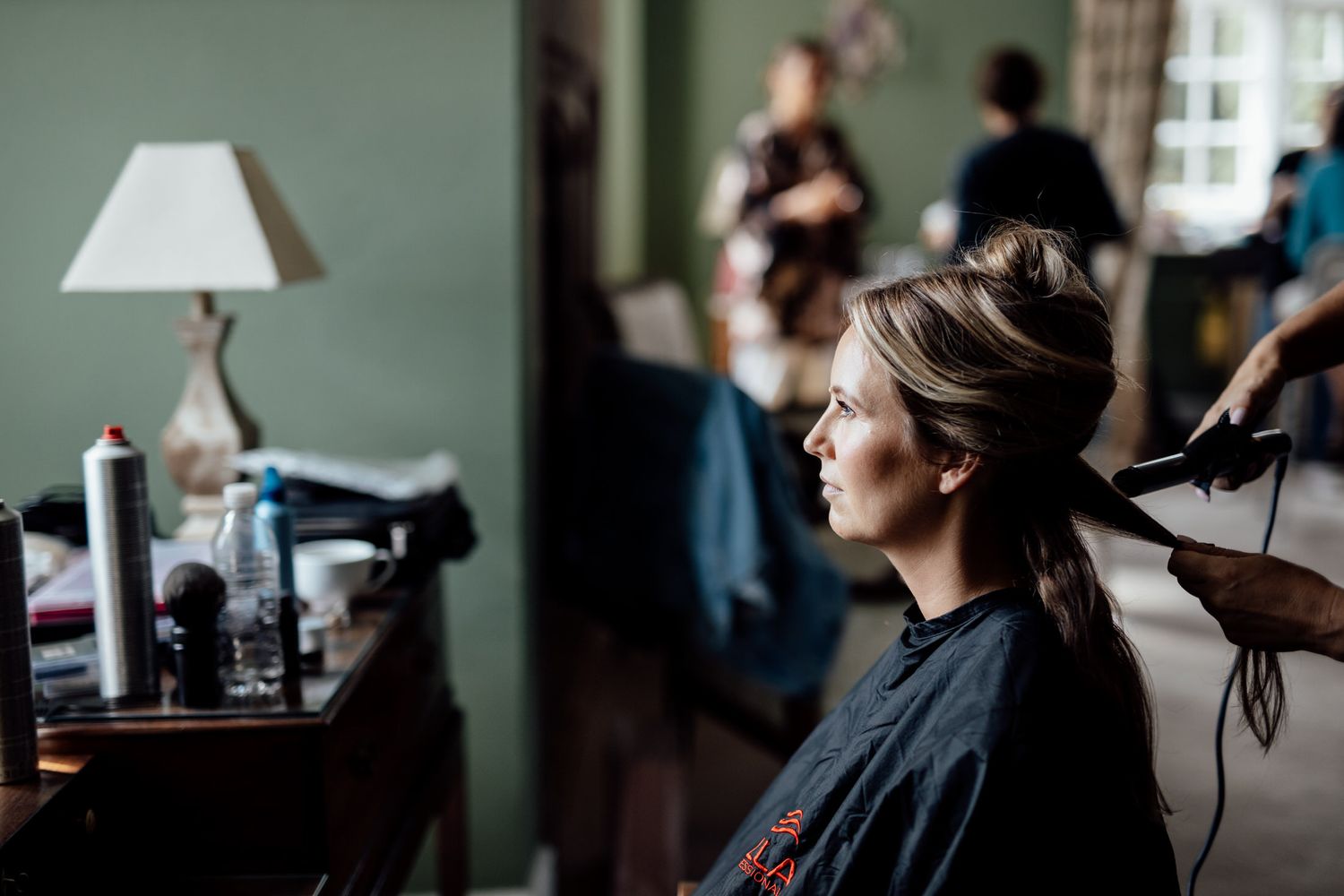 Interior preparation scene with makeup and hair styling in a bright room with natural light.
