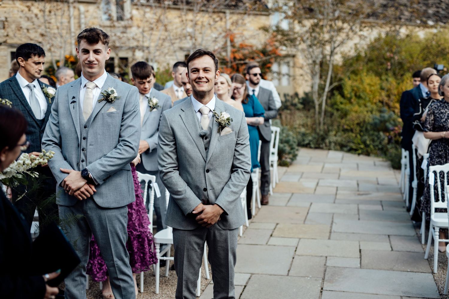 Wedding party members in gray suits stand together during an outdoor ceremony.
